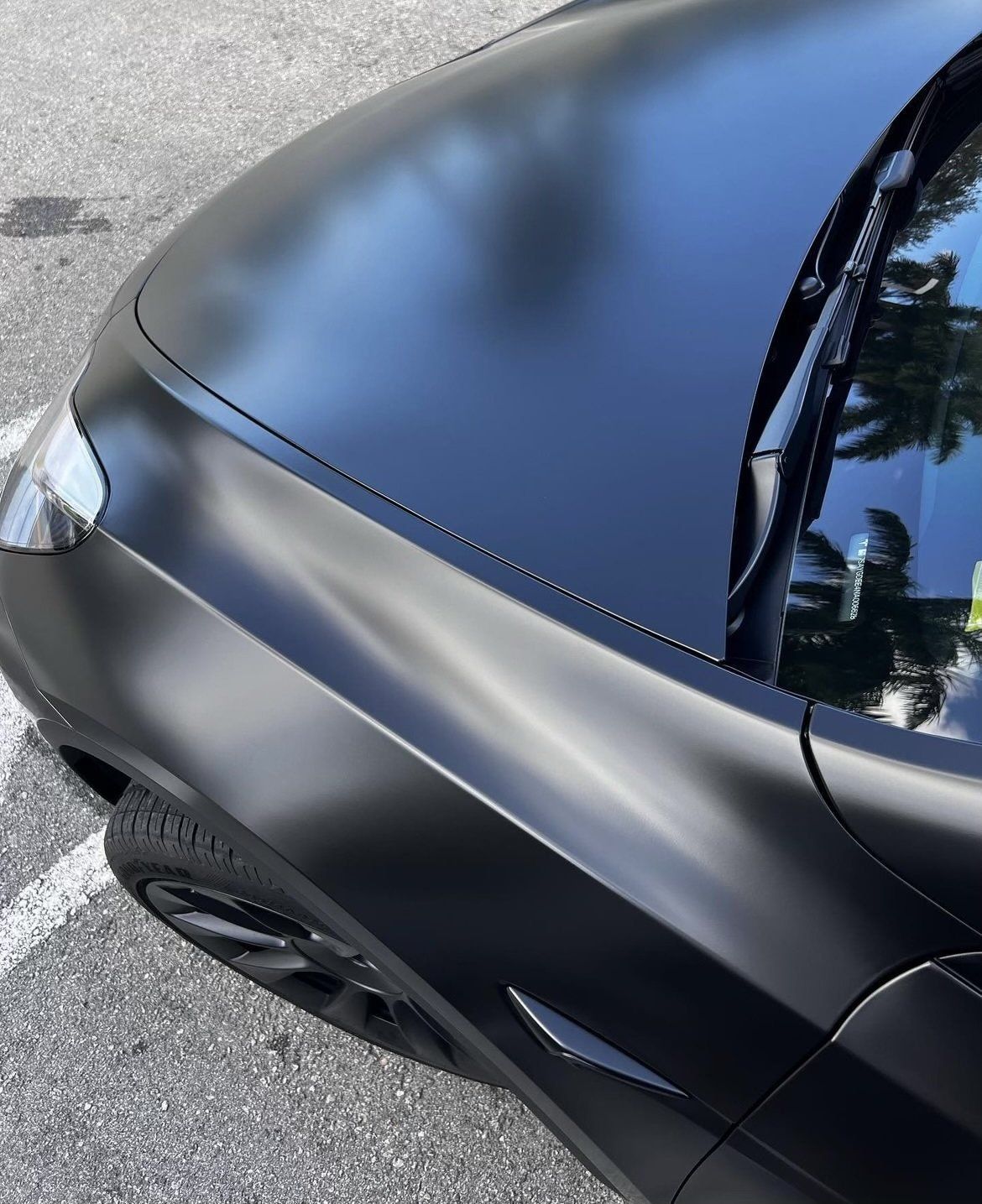 Sleek, matte black car hood, corner view, outdoors.