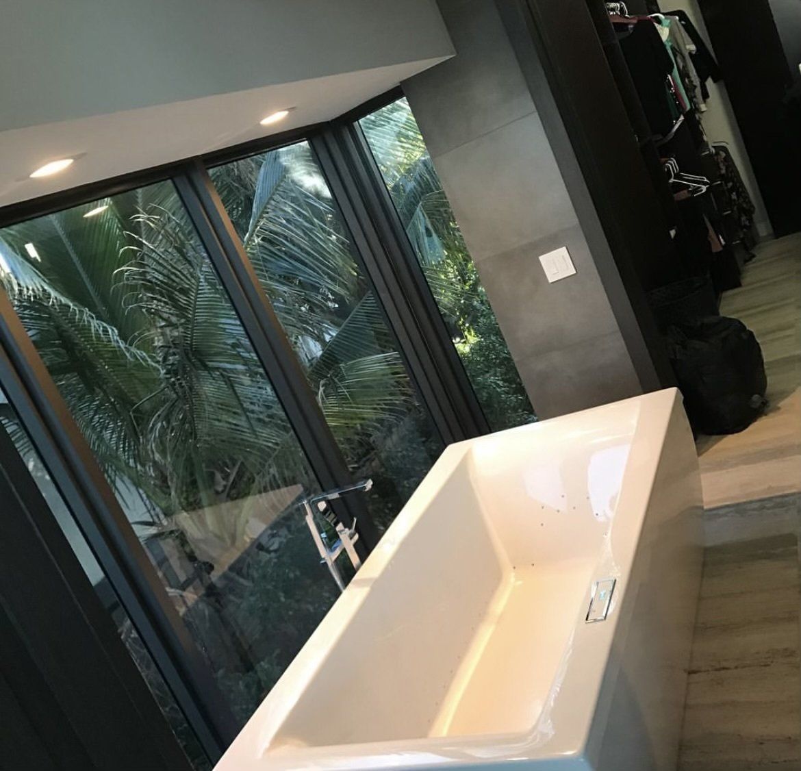 White bathtub by a large window with a view of tropical foliage.