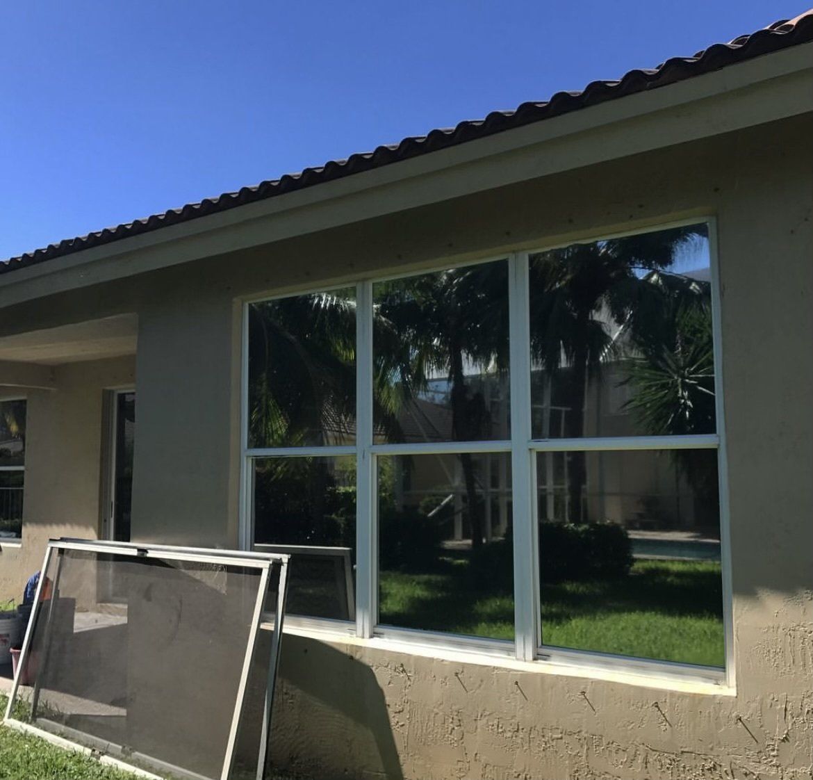 Exterior view of a house with a large window and a screen, reflecting trees and sky.