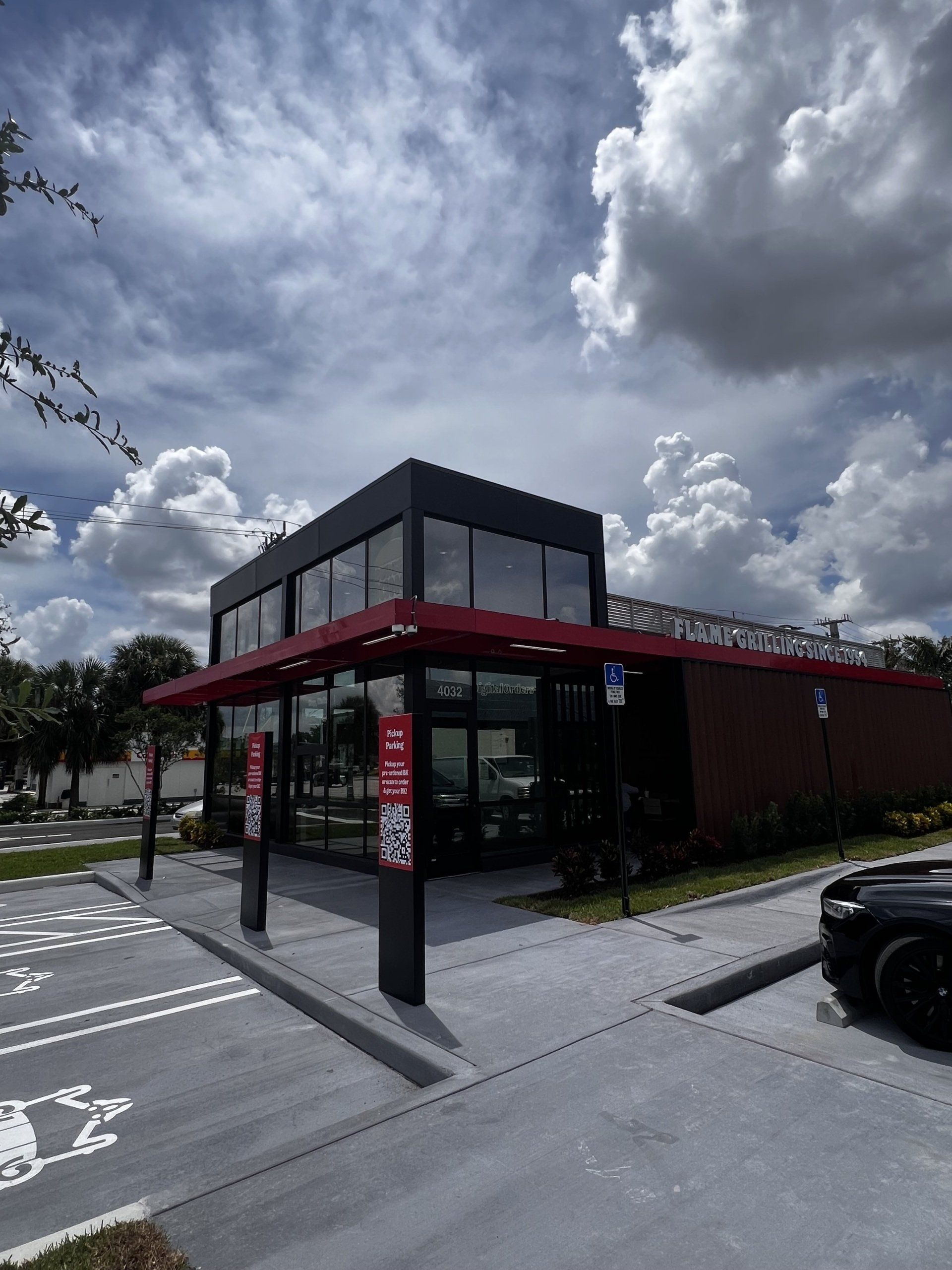 KFC restaurant exterior with a drive-thru. Black building with red accents, overcast sky, and parking spots.