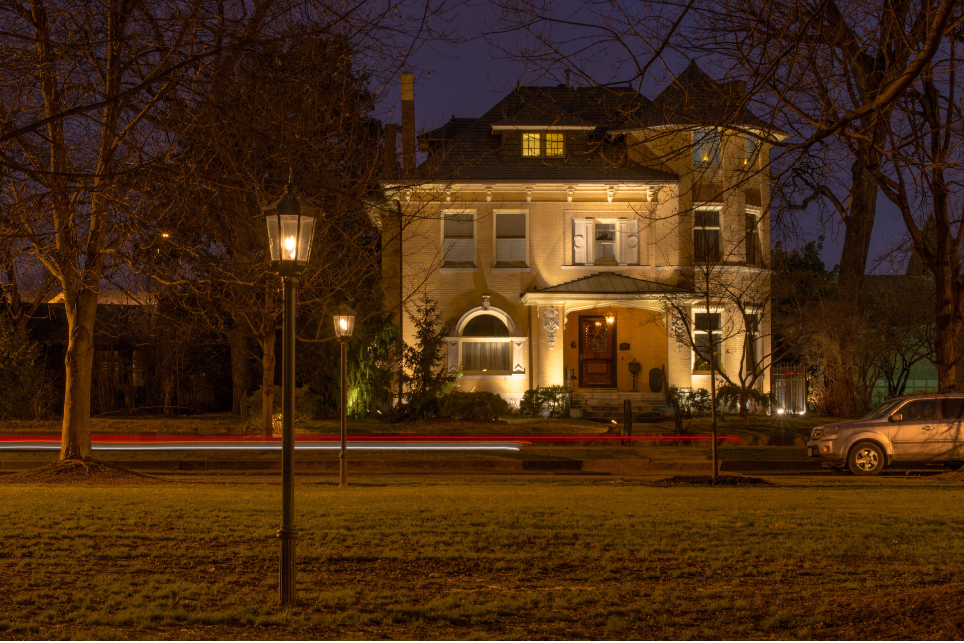 A large house is lit up at night with cars parked in front of it