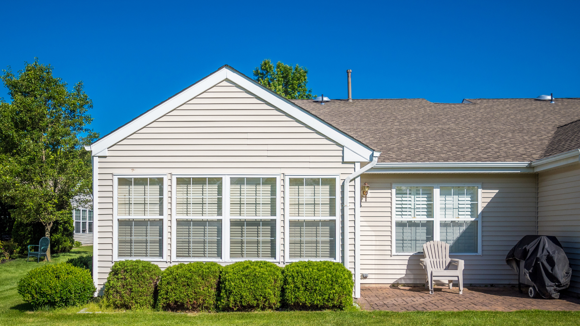 Beige house exterior with windows, green bushes, and a blue sky.