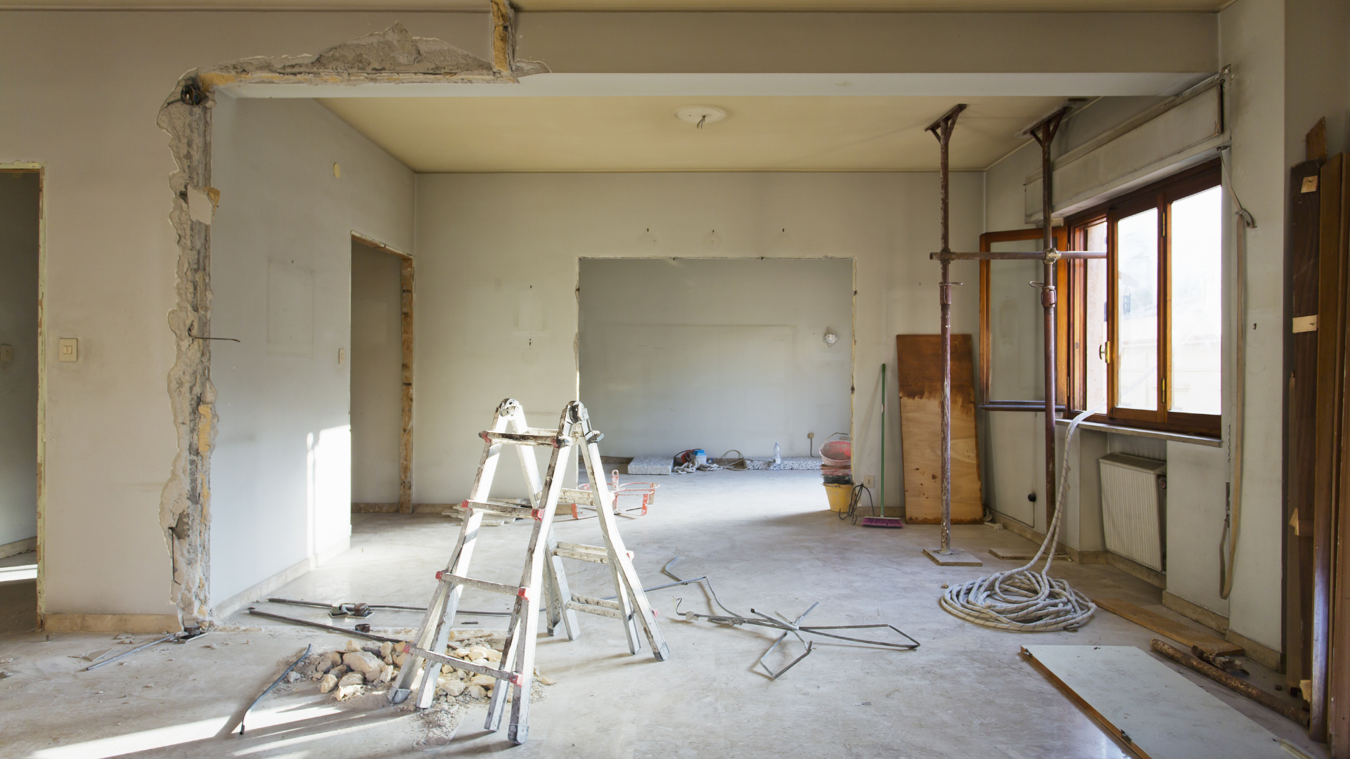 Interior room undergoing renovation; exposed supports, ladder, debris, and open doorways.