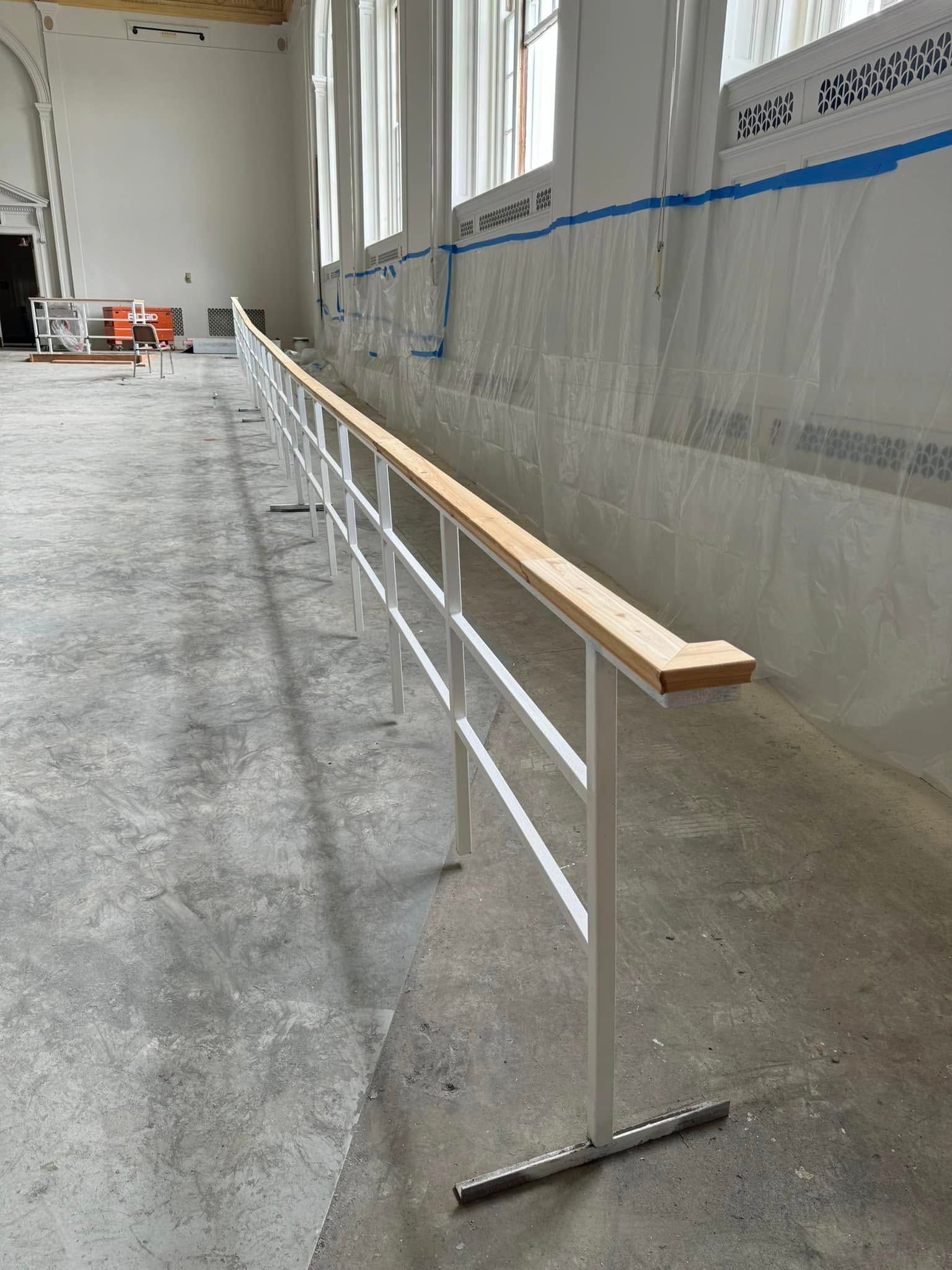 A long white railing with a wooden top is in a room with a lot of windows.