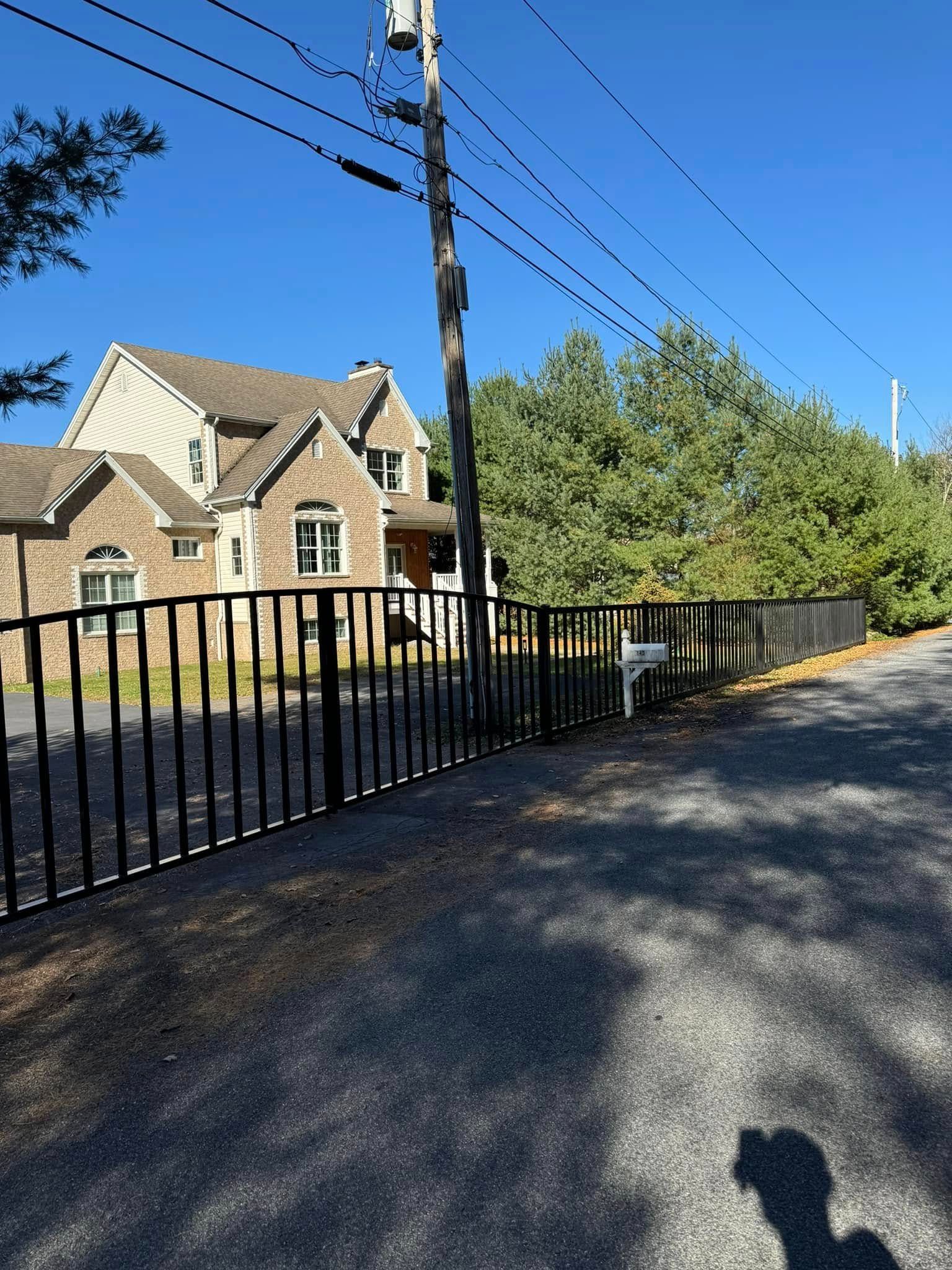 A brick house with a metal fence surrounding it is sitting on the side of a road.