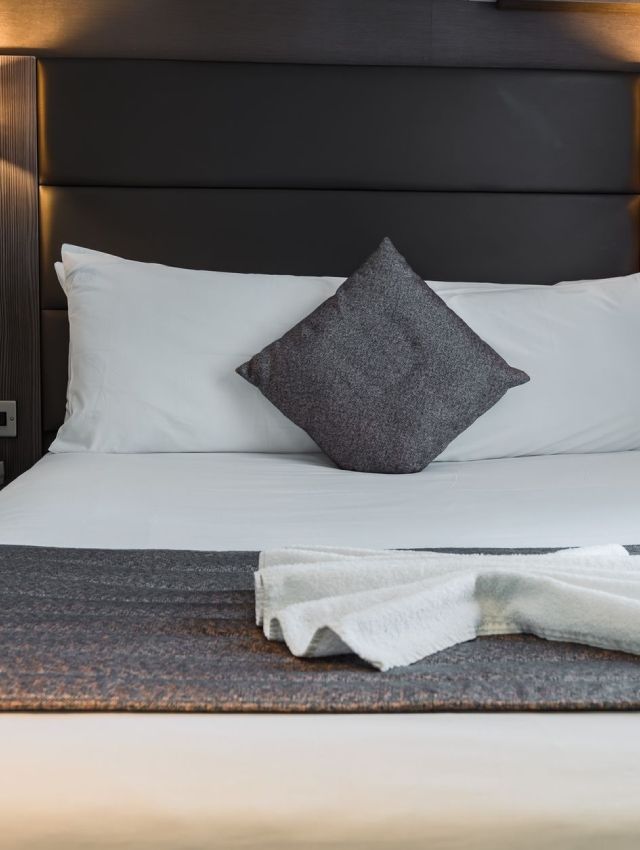 una cama con sábanas blancas y una almohada gris