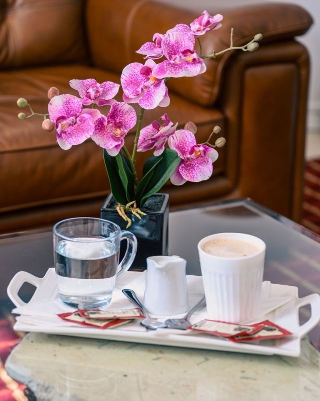 una bandeja con una taza de café y un jarrón de flores rosas sobre una mesa.