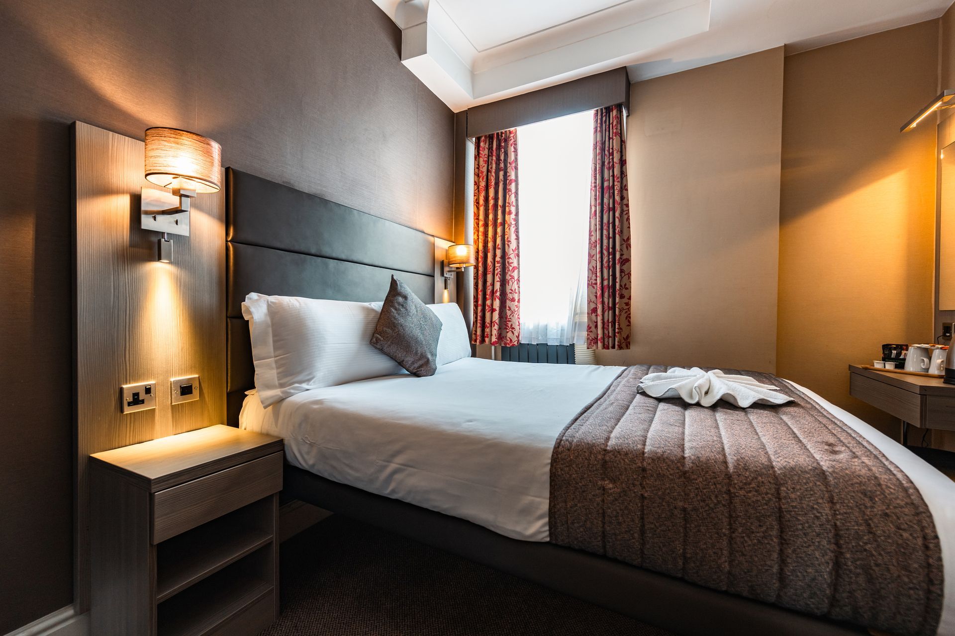 A hotel room with a bed , nightstand , mirror and window.