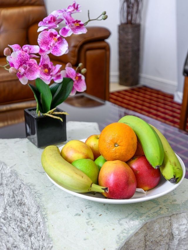 a bowl of fruit sits on a table next to a vase of flowers.jpg