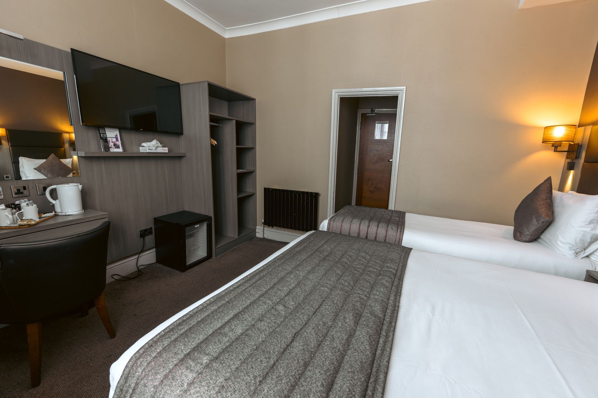 una camera d'albergo con due letti, una scrivania e un televisore.