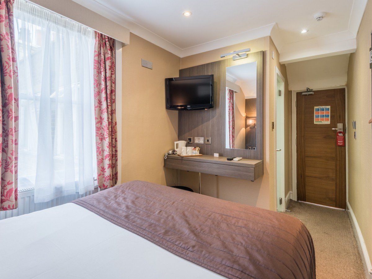 una camera d'albergo con letto, cassettiera, televisione e specchio.