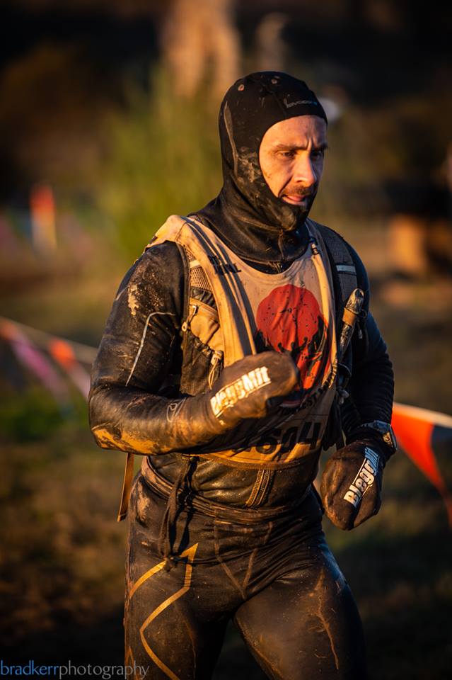 A man in a wet suit is running through a muddy field.