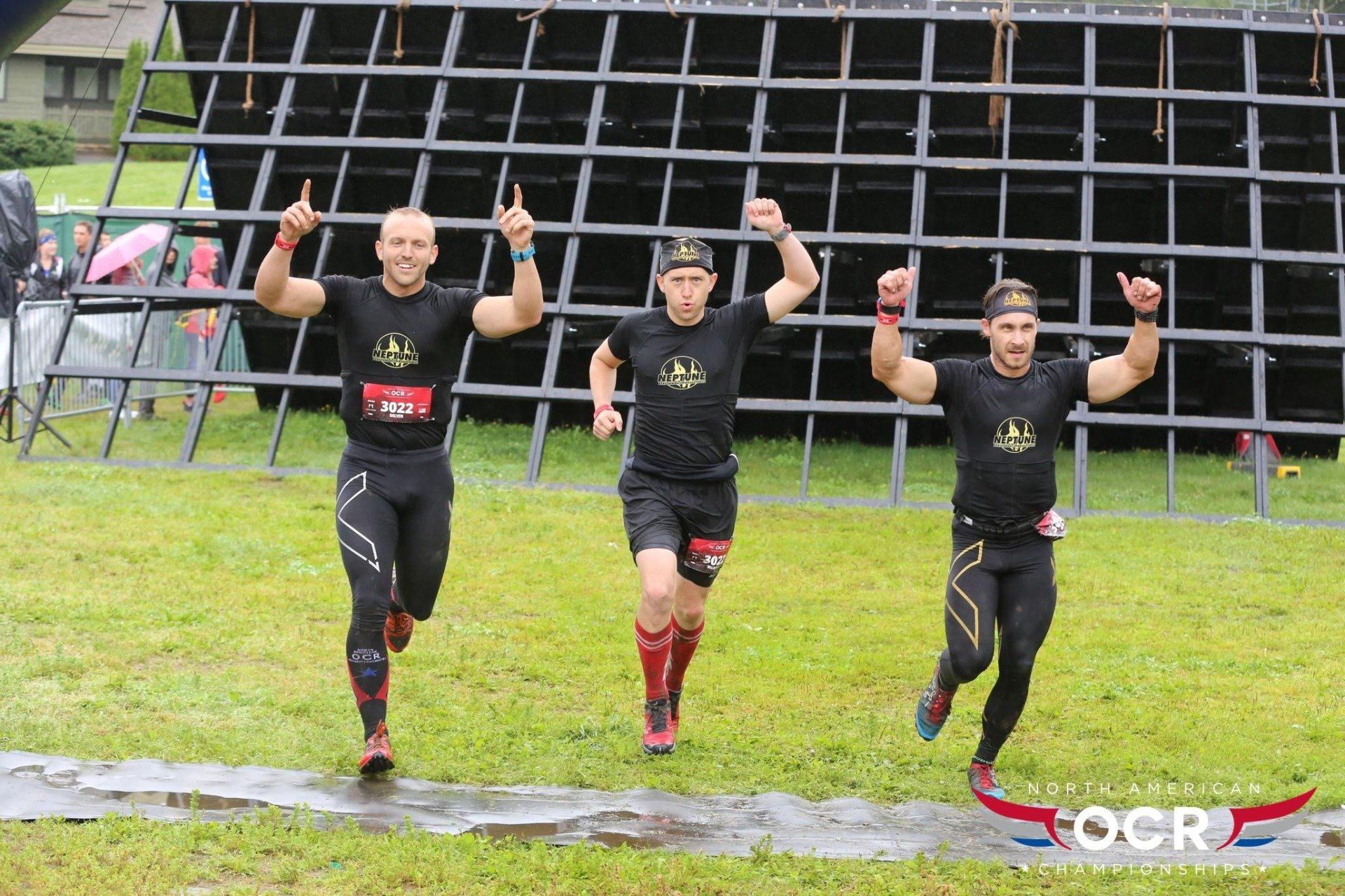 Three men are running in a field with their arms in the air.