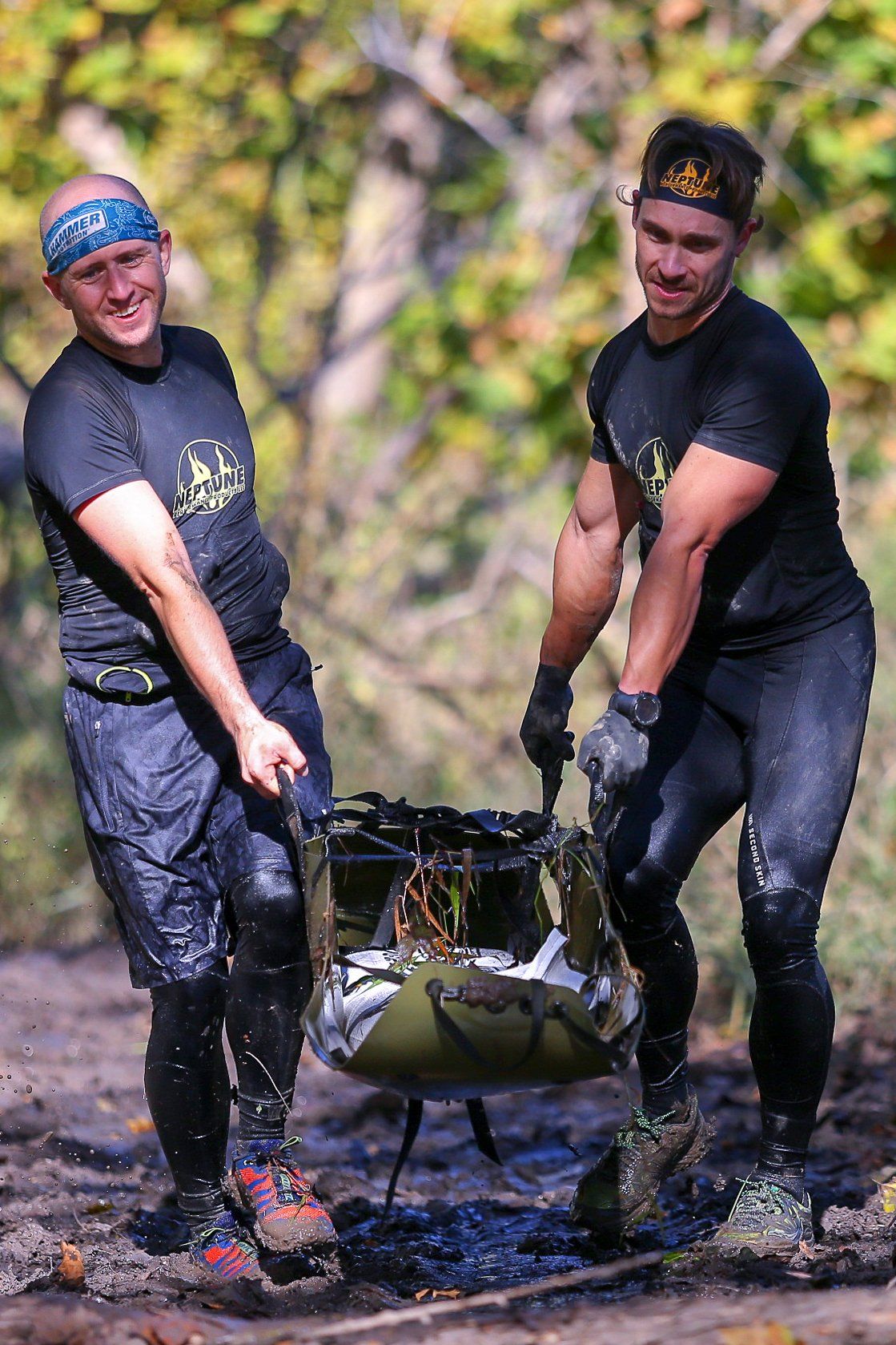 Two men are carrying a bag through the mud.