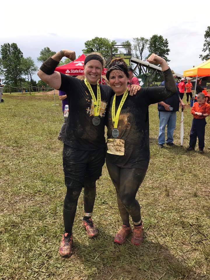 Two women are posing for a picture in a muddy field.