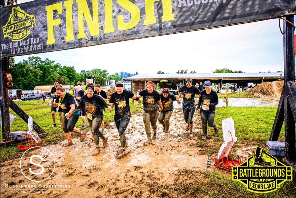 A group of people are running through a muddy field.