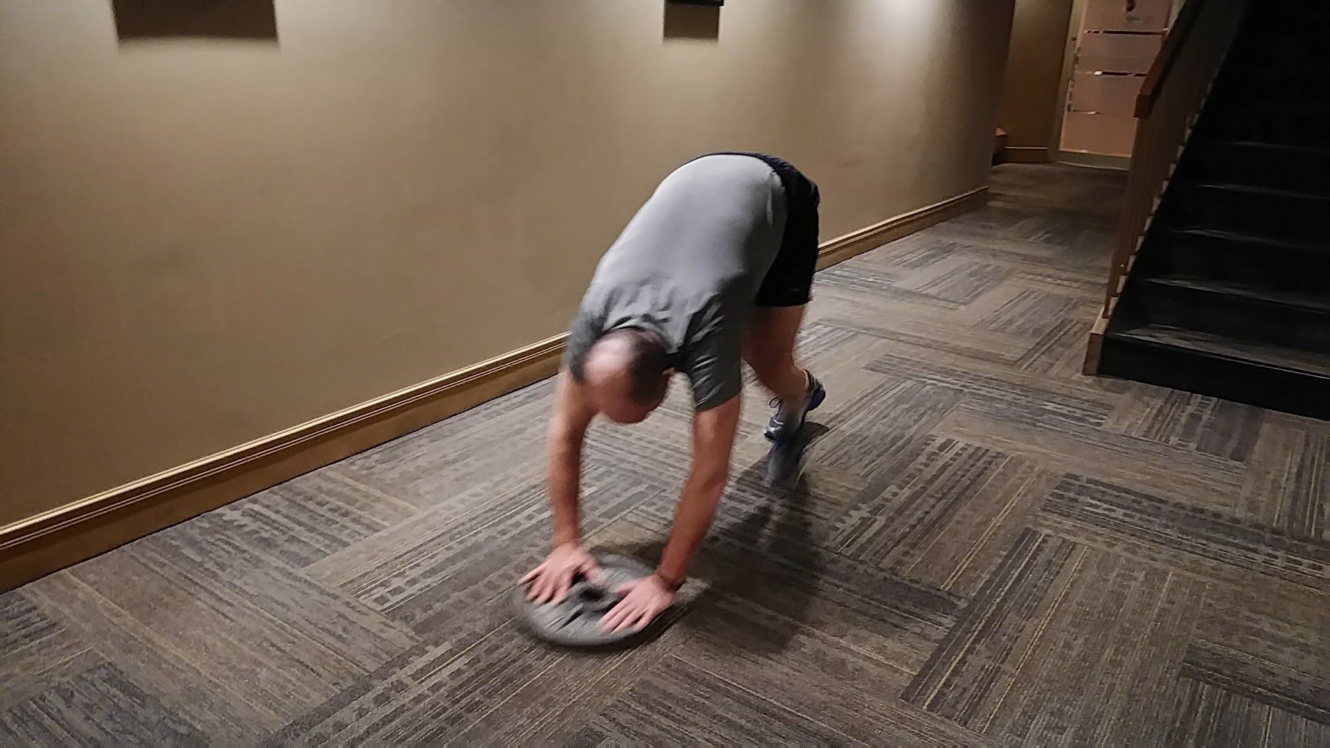 A man is doing push ups on a weight plate in a hallway.