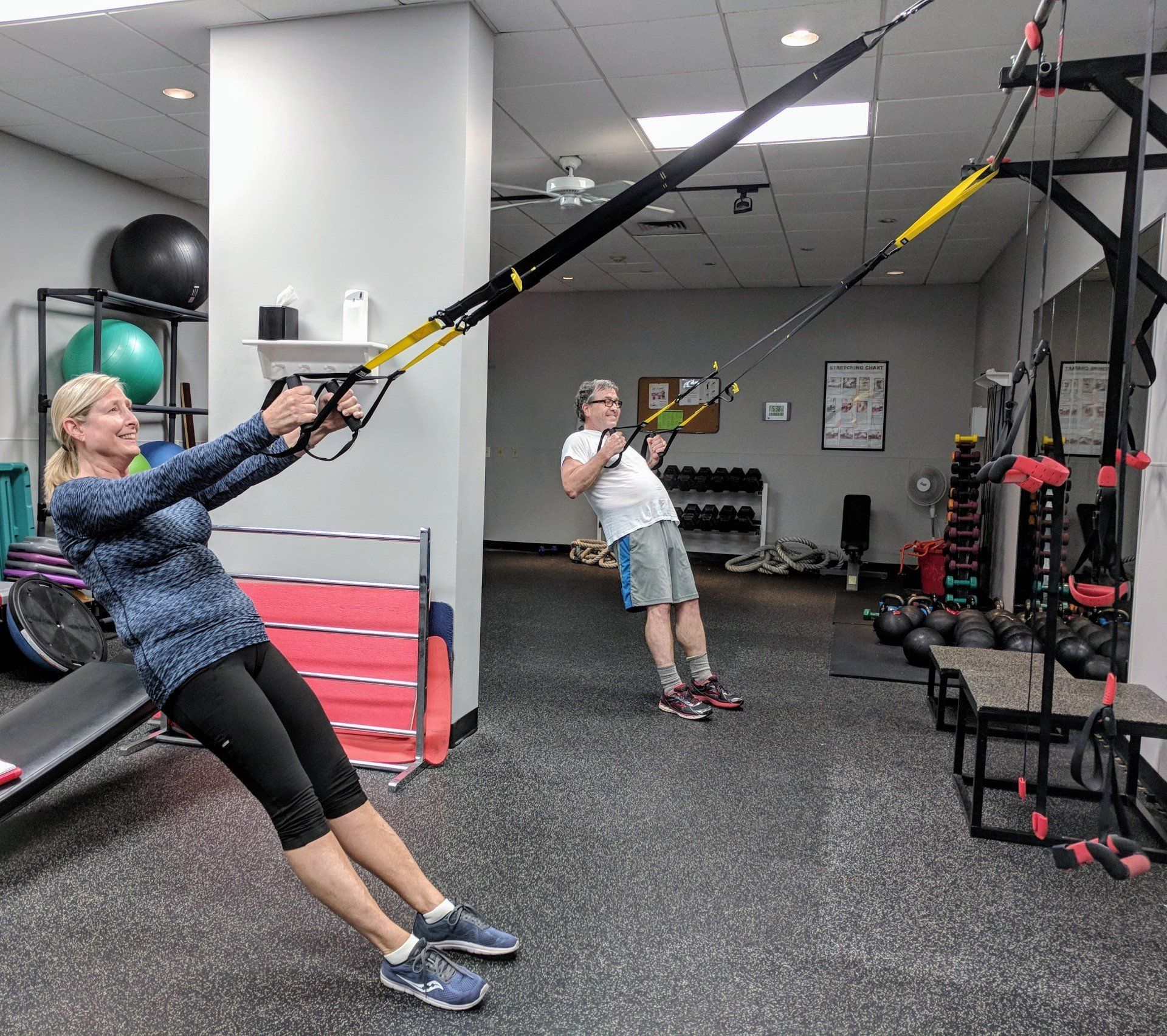 A man and a woman are doing trx exercises in a gym.