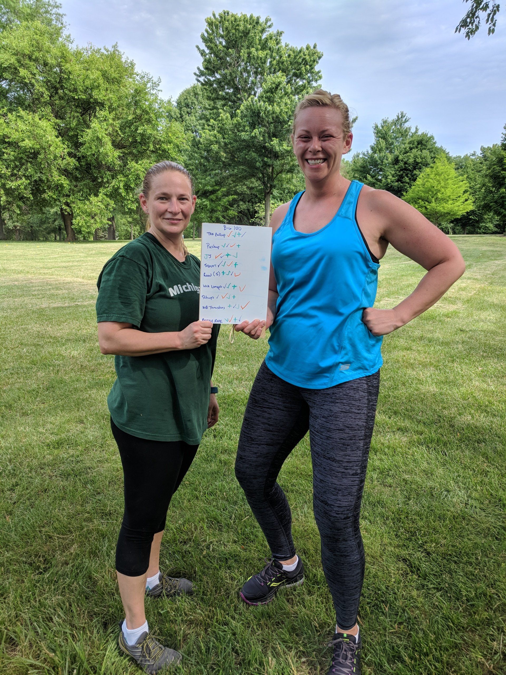 Two women are standing in a grassy field holding a piece of paper.