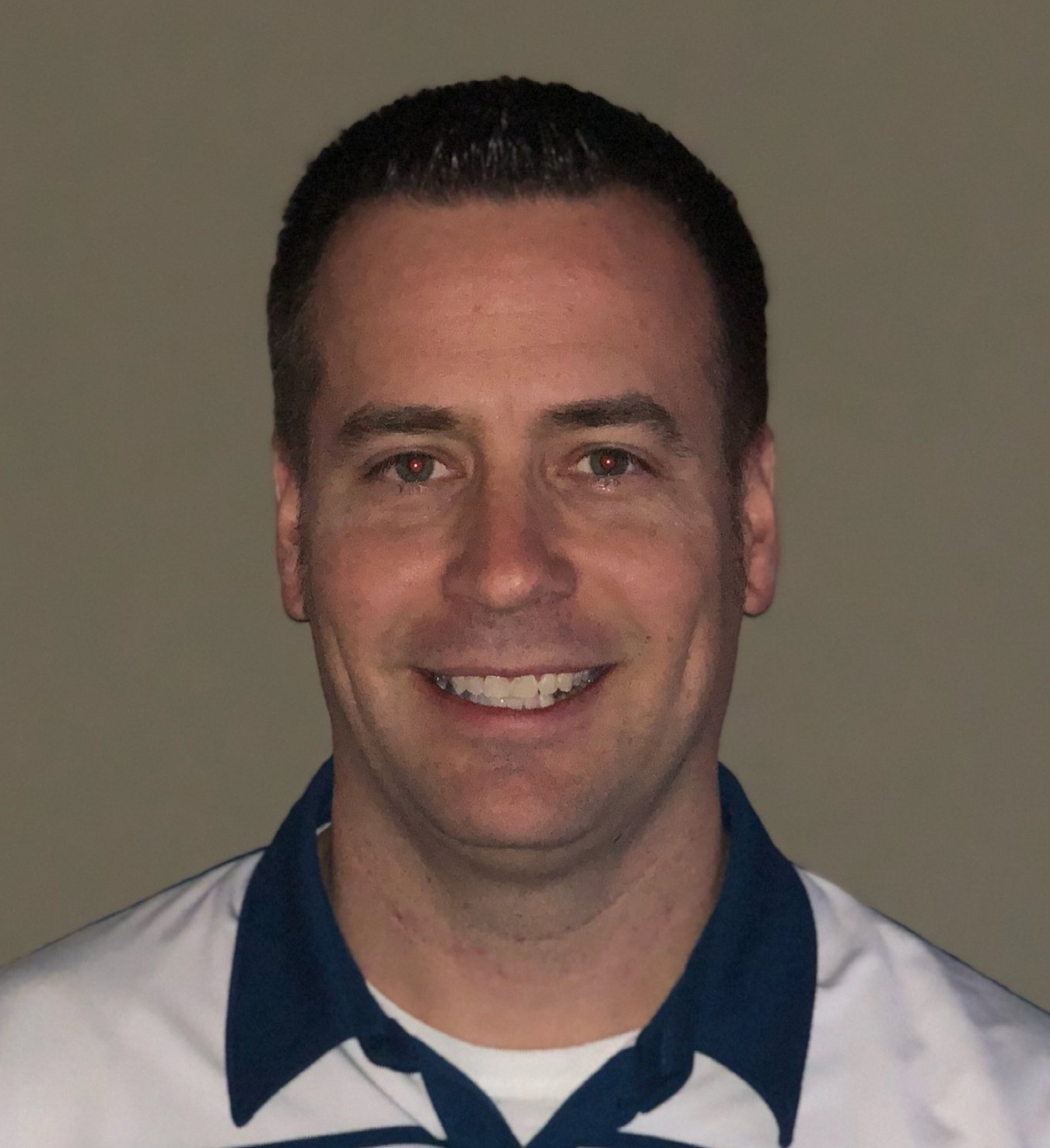 A man wearing a white shirt with a blue collar smiles for the camera