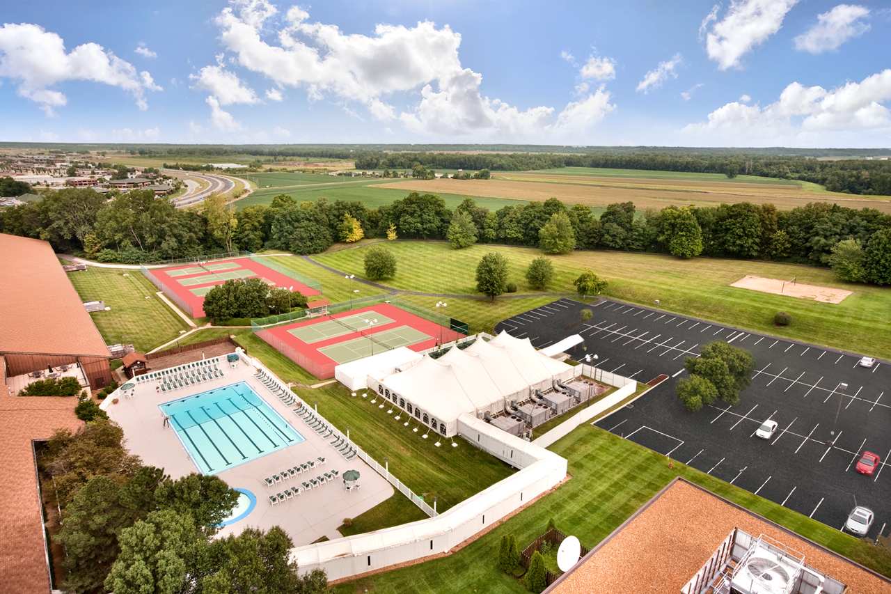An aerial view of a school with a swimming pool , tennis courts , and parking lots.