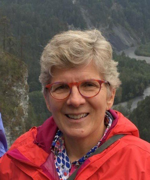 A woman wearing glasses and a red jacket smiles for the camera