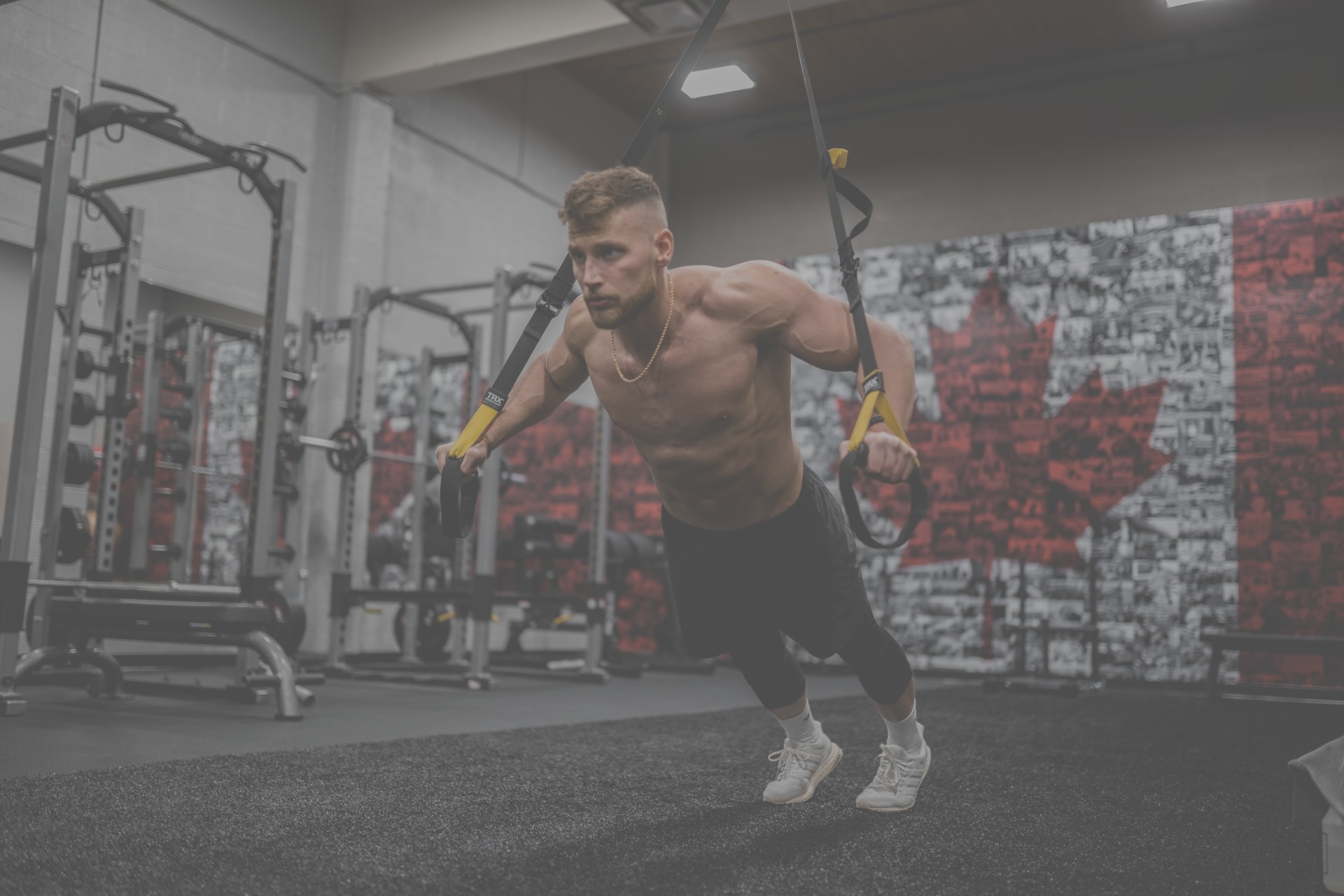 A shirtless man is doing push ups on a trx in a gym.