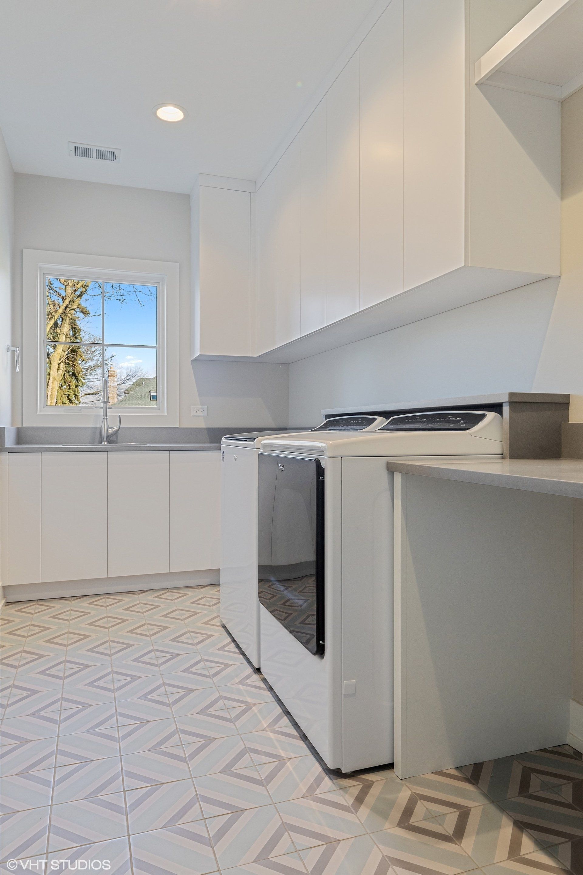 A kitchen with white cabinets , a stove , a sink , and a window.
