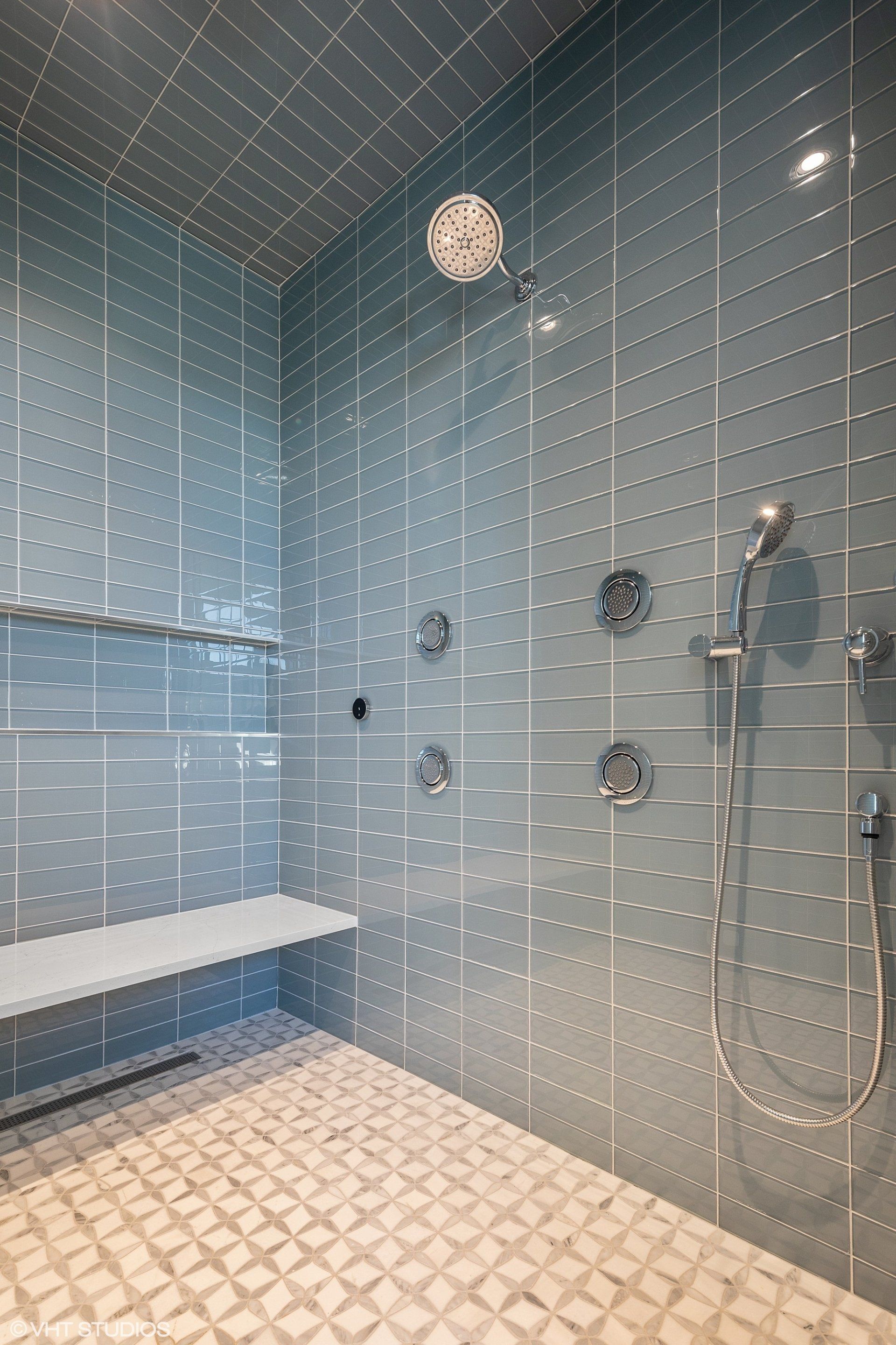 A bathroom with blue tiles and a walk in shower with a bench.