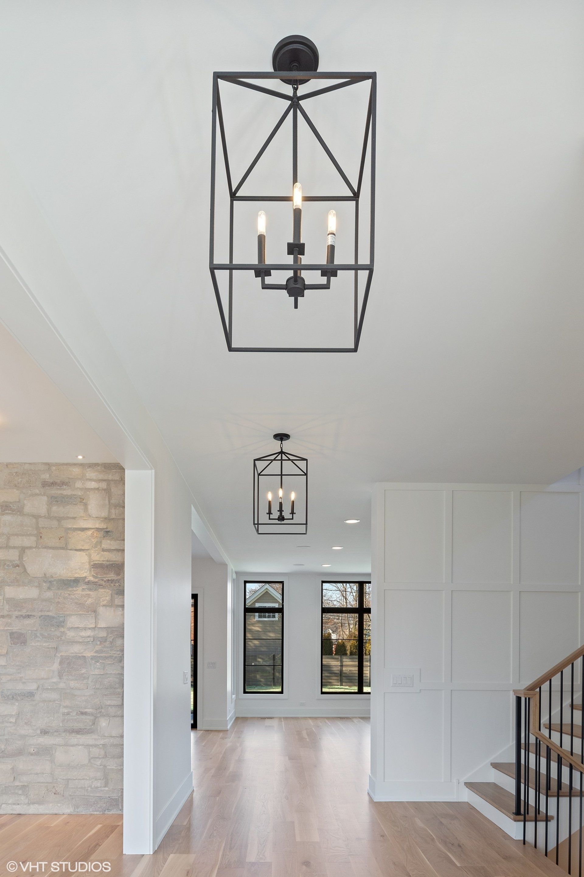 A black chandelier is hanging from the ceiling of a hallway in a house.