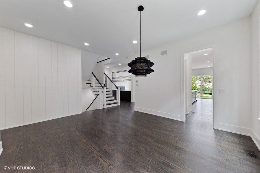 An empty living room with hardwood floors and a black chandelier hanging from the ceiling.