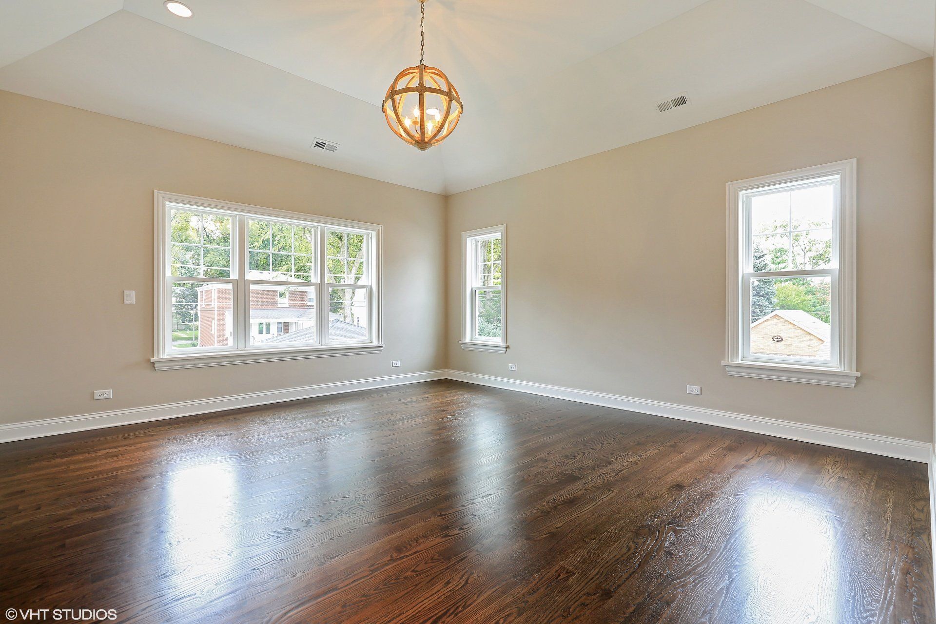 A large empty room with hardwood floors and a chandelier hanging from the ceiling.