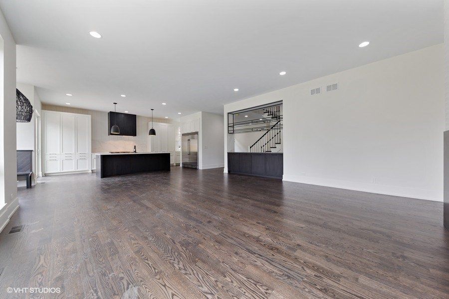 An empty living room with hardwood floors and a kitchen in the background.