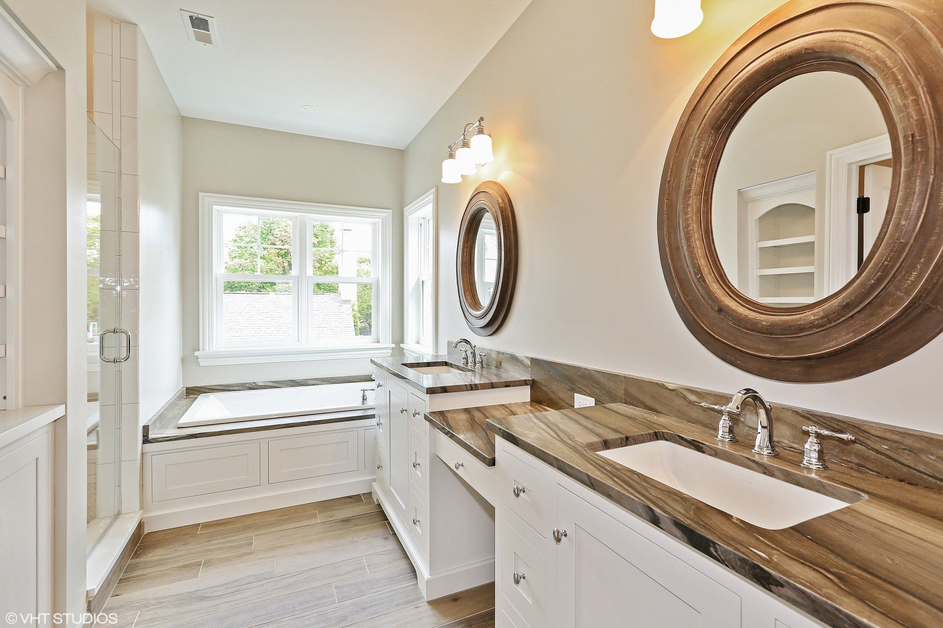 A bathroom with two sinks , two mirrors and a tub.