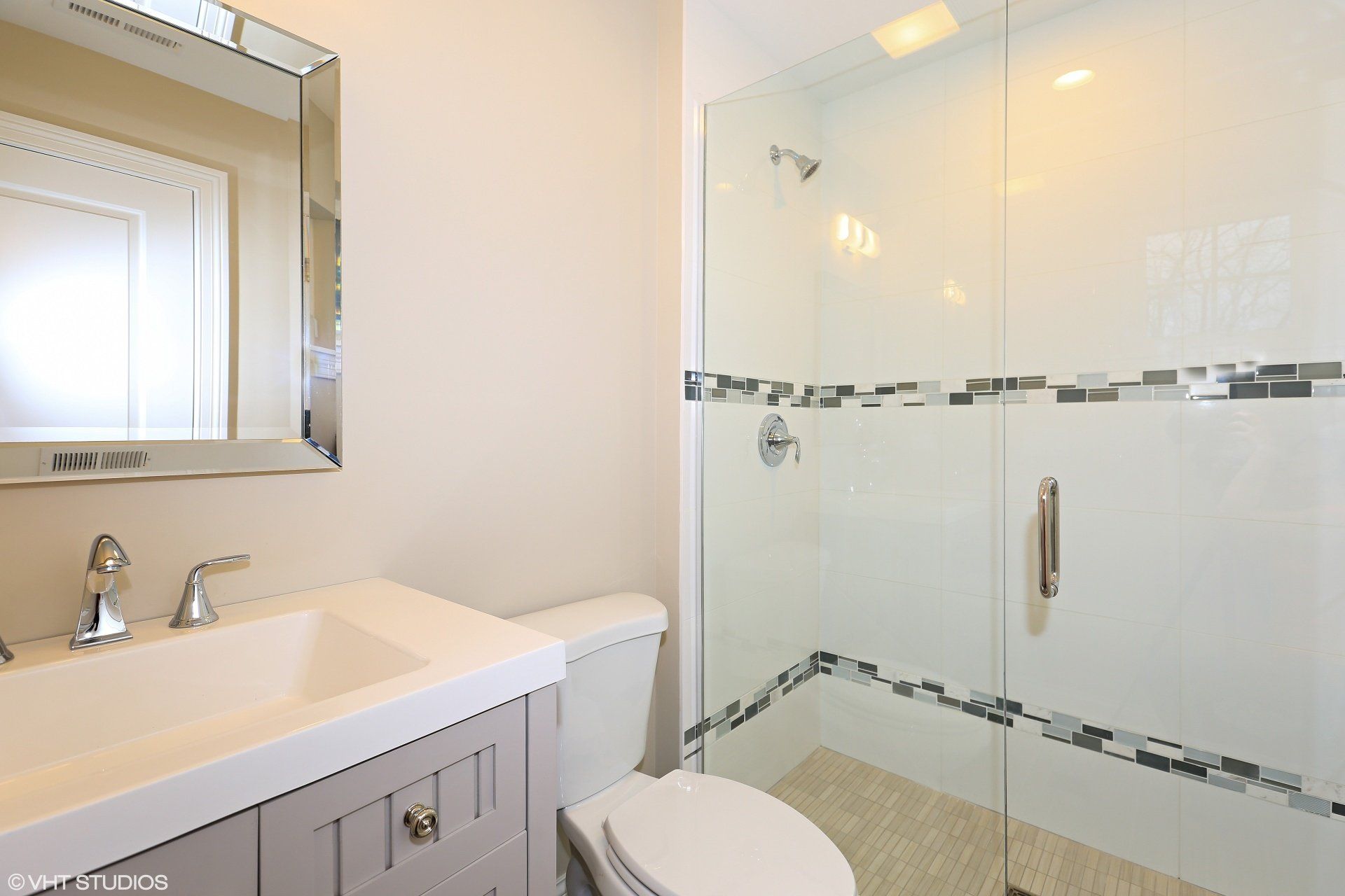 A bathroom with a toilet , sink , mirror and walk in shower.