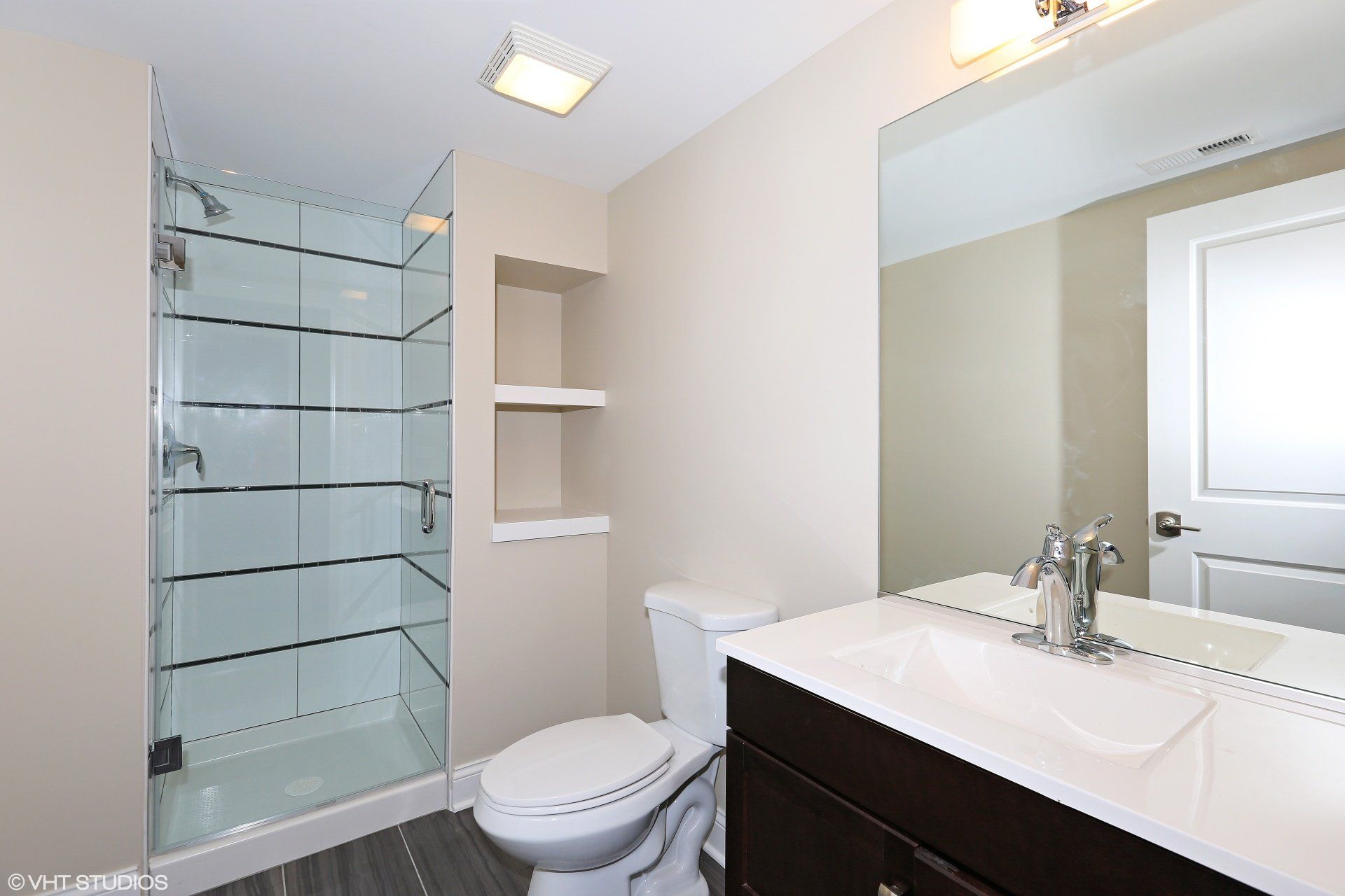 A bathroom with a toilet , sink , shower and mirror.