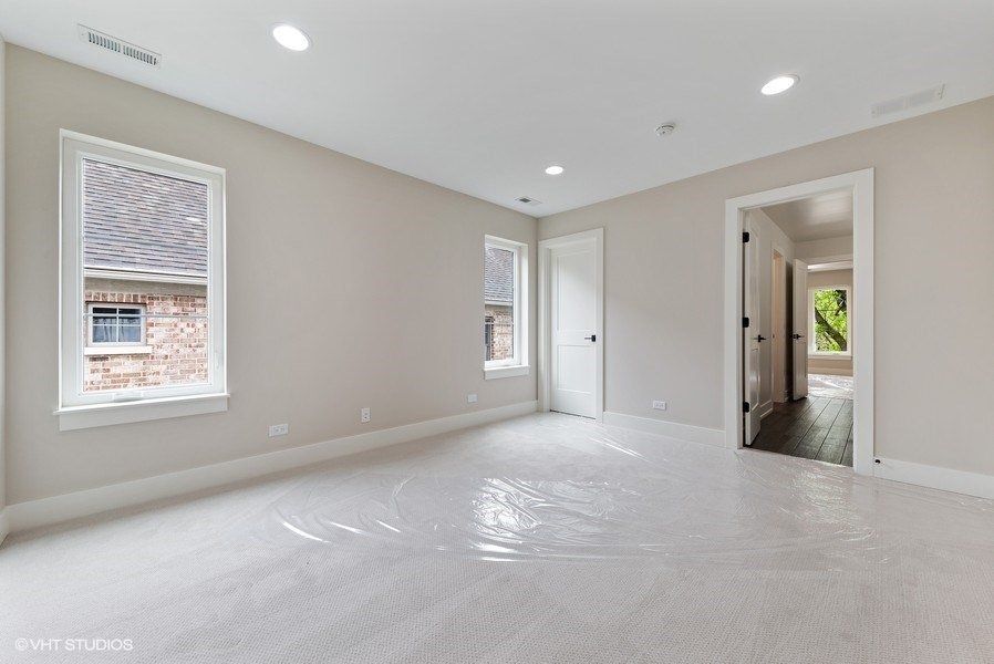 An empty bedroom with a carpeted floor and two windows.