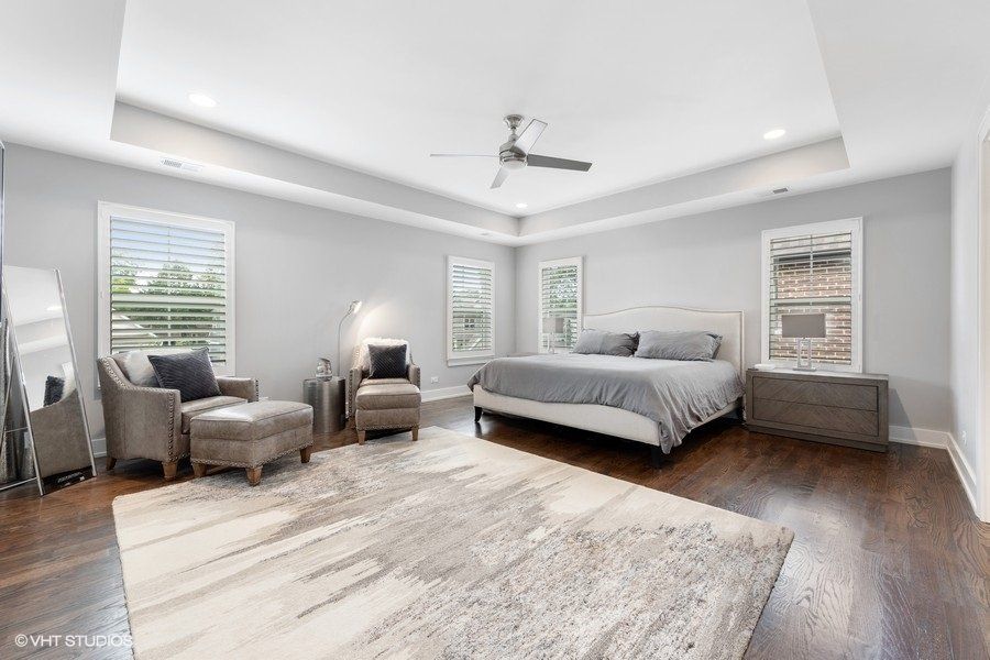 A large bedroom with a bed , chairs , ottoman and ceiling fan.