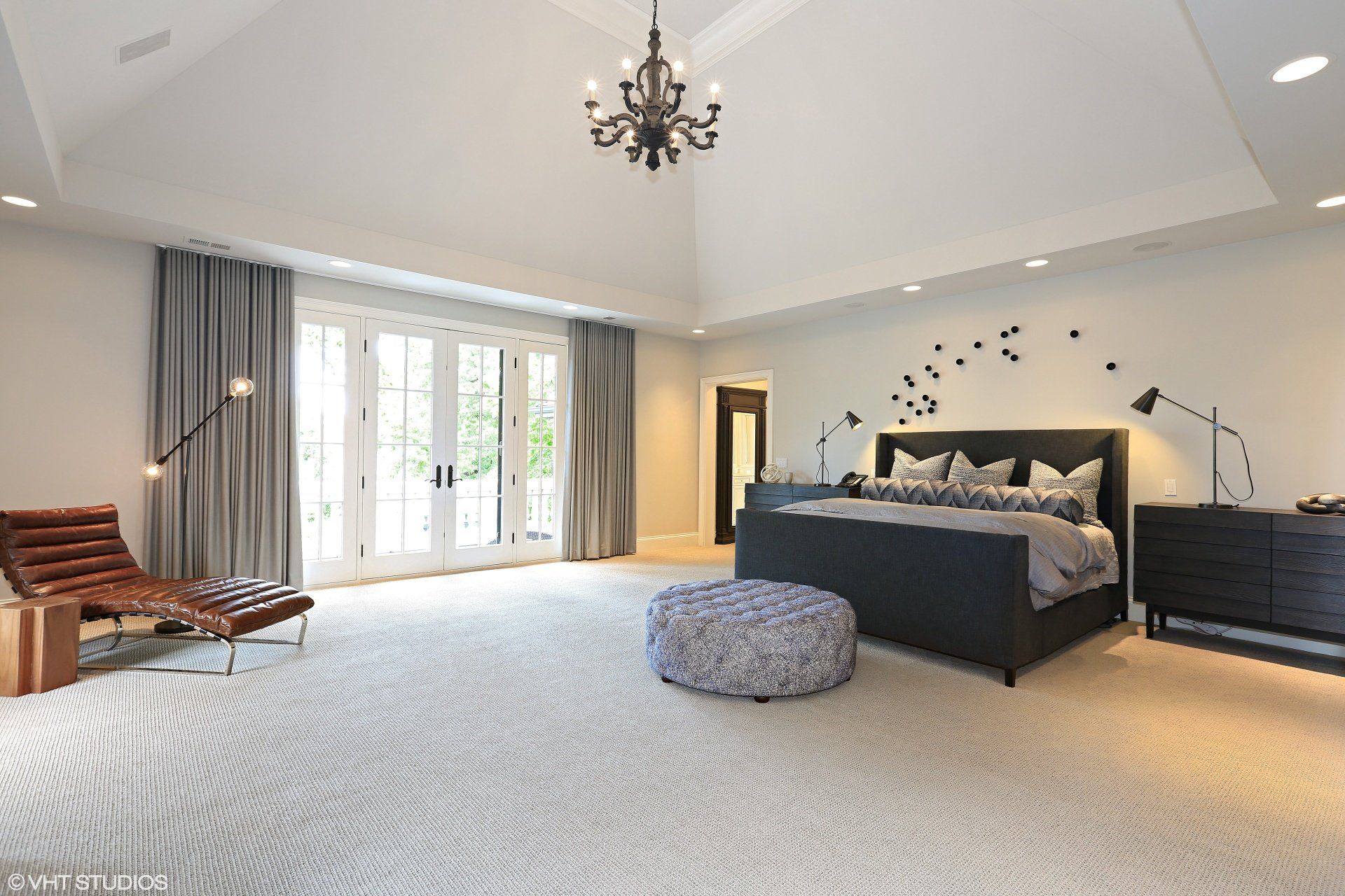 A bedroom with a large bed , ottoman , chair and chandelier.
