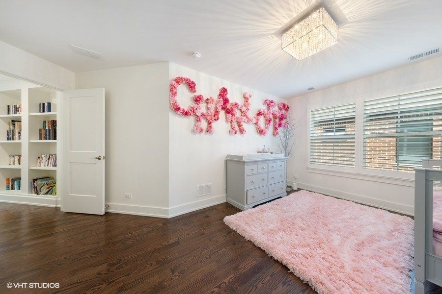 A bedroom with a pink rug , a bed , a dresser , and a painting on the wall.