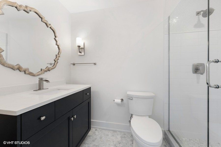 A bathroom with a toilet , sink , mirror and walk in shower.