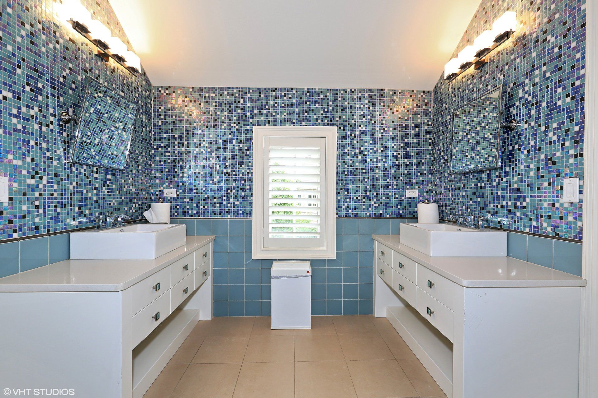 A bathroom with blue tiles and two sinks and a window