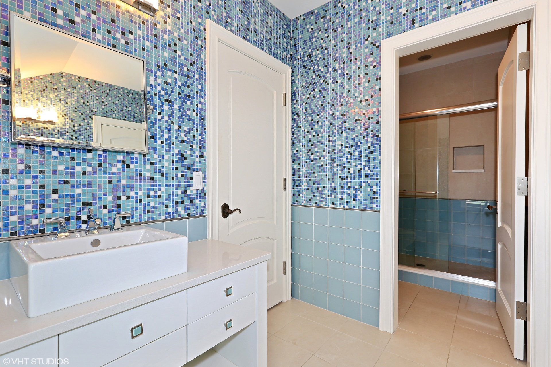 A bathroom with blue tiles and a sink and mirror
