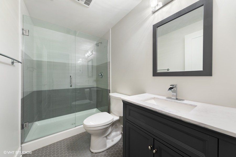 A bathroom with a toilet , sink , mirror and walk in shower.