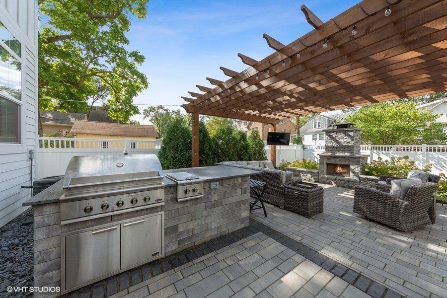 A patio with a grill and a pergola over it.