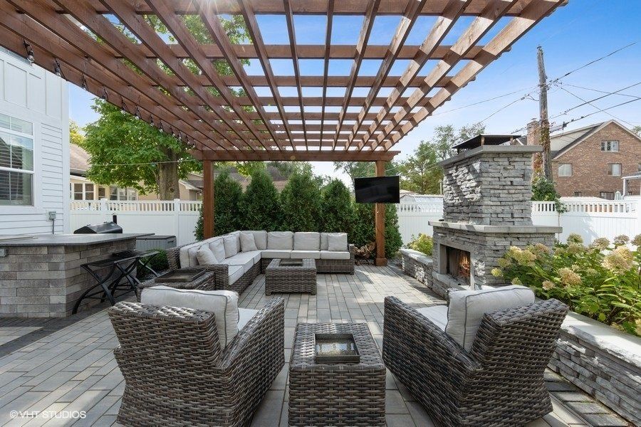 A patio with wicker furniture and a fireplace under a pergola.