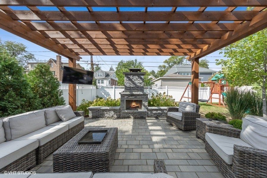 A patio with wicker furniture and a fireplace under a pergola.