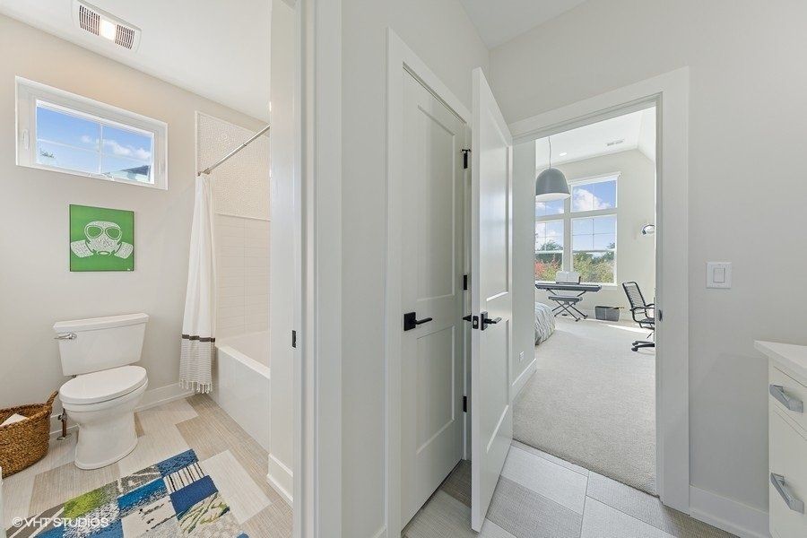 A bathroom with a toilet , bathtub , sink and door leading to a bedroom.