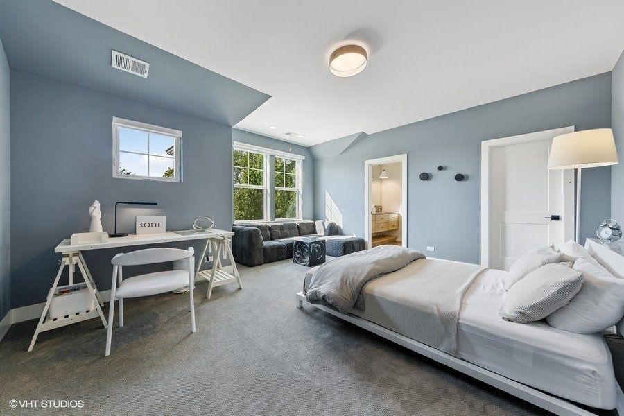 A bedroom with a bed , desk , chairs and a window.