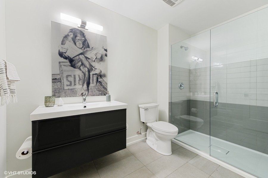 A bathroom with a toilet , sink , shower and a painting on the wall.